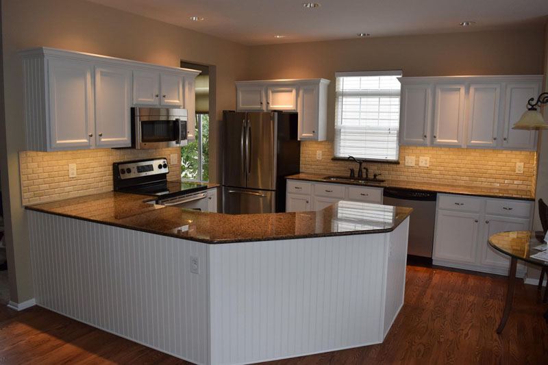 White painted kitchen cabinets with a white beadboard island and dark granite