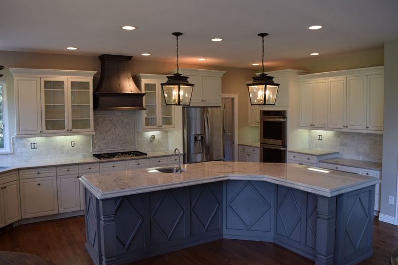 White painted kitchen cabinets with a navy blue island and lantern pendants