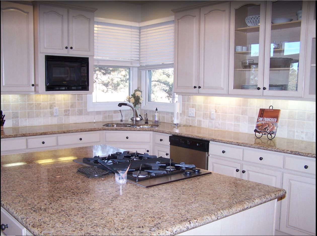 White painted cabinets with glass-front uppers and a granite island with a cooktop