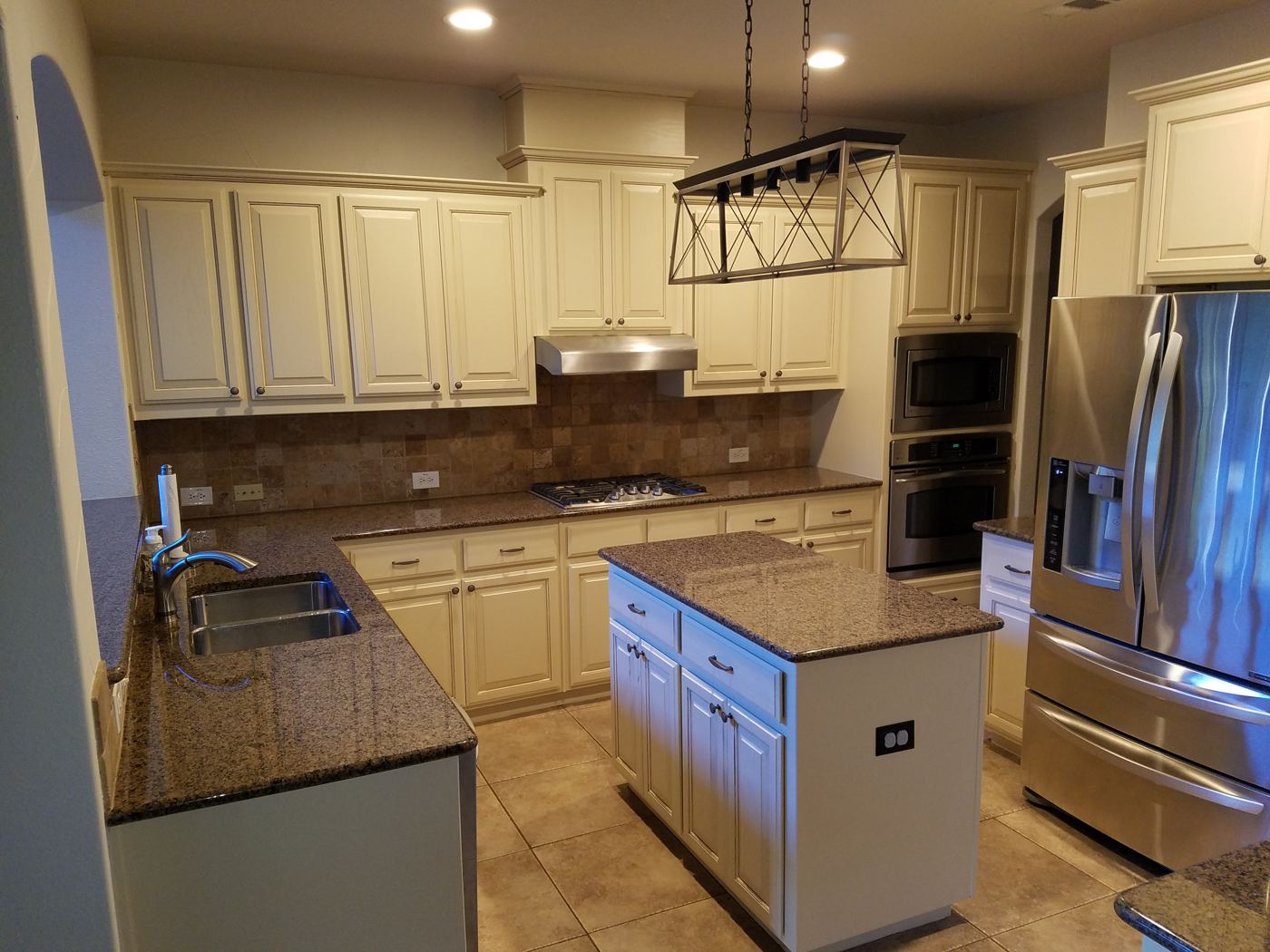 Cream painted kitchen cabinets with a gray island and a tile backsplash