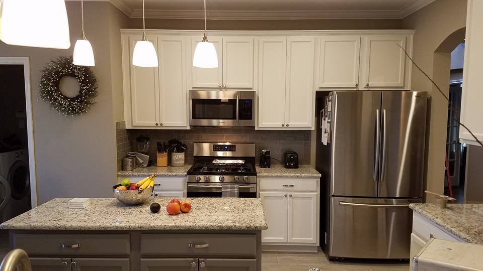 White painted cabinets with a gray island under three glass pendants