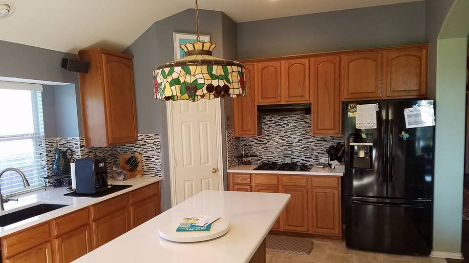 Oak cabinets around a black refrigerator, before painting