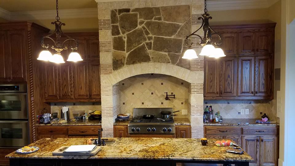 Dark stained cabinets on both sides of a stone range hood arch, before