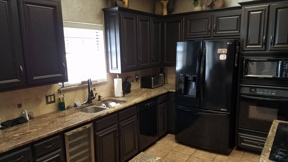 Kitchen cabinets painted black with tan granite and a travertine backsplash