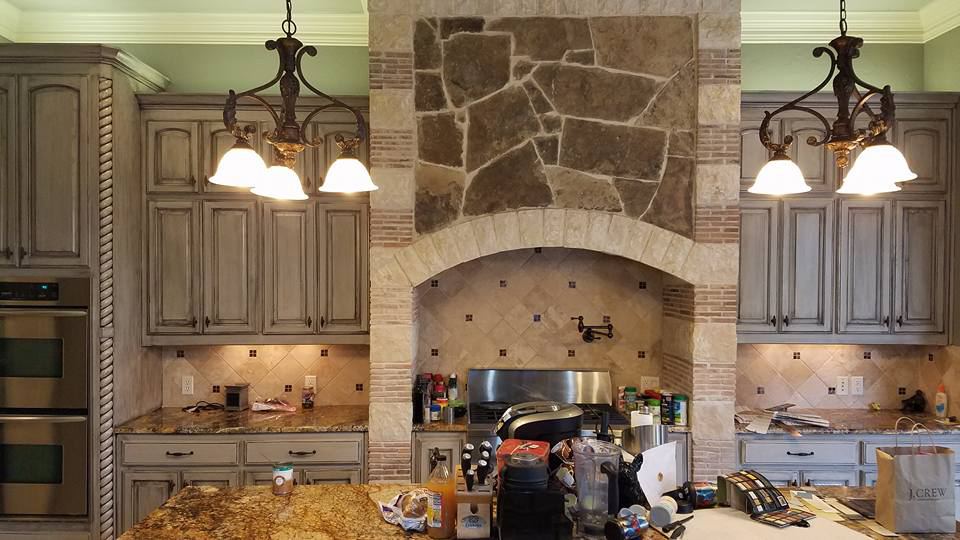 The same cabinets refinished in a gray glaze beside the stone hood, after