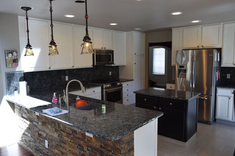 White painted cabinets with a black island and a stacked-stone bar